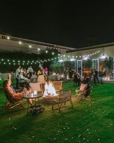 a group of people sitting around a fire pit on top of a lush green field