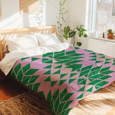 a bed with a green and pink blanket on top of it next to a window