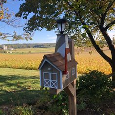 a mailbox with a flag on top in front of a tree and farm field