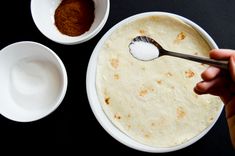 a person spooning sugar into a bowl with tortilla batter in it and two bowls on the side