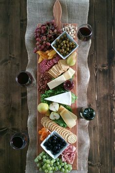 a wooden platter filled with different types of cheese and meats next to two glasses of wine