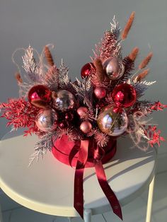 a vase filled with christmas ornaments on top of a white table next to a red ribbon