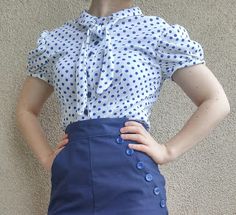 a woman wearing a polka dot blouse and blue skirt