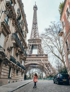 a woman standing in front of the eiffel tower on a cobblestone street