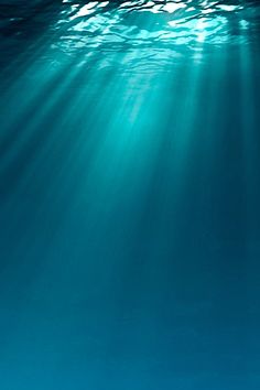 an underwater view of the ocean with sunlight coming through the water's surface and light shining