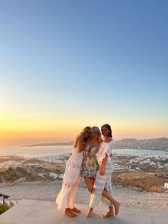 three women are standing on the edge of a cliff with their arms around each other