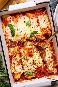 a casserole dish with meat, cheese and spinach on the side next to bread