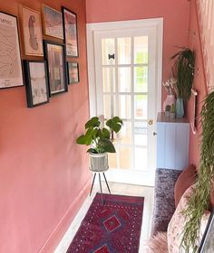 a hallway with pink walls and pictures on the wall, plants in vases next to door