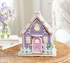 a gingerbread house sitting on top of a wicker table next to a vase with flowers