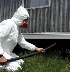 a man in a white suit is using a hose to clean the grass outside his house