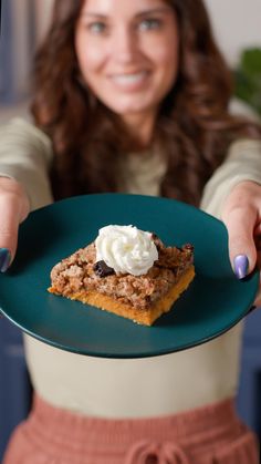 a woman holding a plate with a piece of cake on it and whipped cream on top