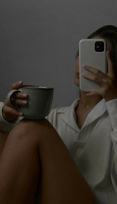 a woman is holding a cup and taking a selfie with her phone while sitting on the floor