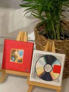 two paintings on easels with a potted plant in the background and a wicker basket