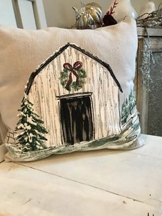 a decorative pillow with a barn and christmas tree on the front is sitting on a chair