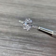 a close up of a diamond ring being held by a metal tool on a wooden surface