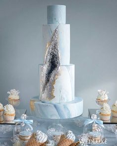 a white and blue cake sitting on top of a table next to cupcakes