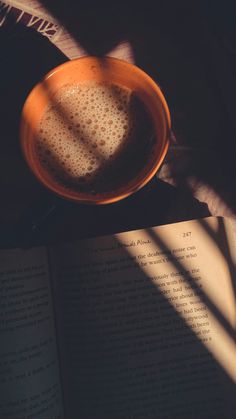 an open book and a cup of coffee on a table next to a bowl with liquid in it