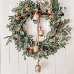 a wreath with bells and greenery hanging on a white wall next to a wooden door