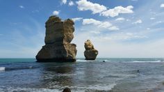 two large rocks sticking out of the ocean next to a beach with people swimming in it