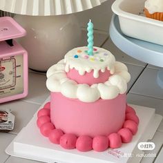 a pink birthday cake sitting on top of a white plate next to a cupcake