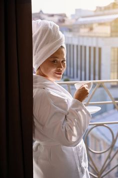 Hotel resident with beverage in hands enjoying urban view in morning stock photo Smiling Woman, Bath Robes For Women, Cup And Saucer, Cityscape, Balcony, Photo Image, Stock Photos, Hotel