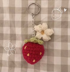 a crocheted strawberry keychain with a flower attached to it, sitting on a checkered table cloth