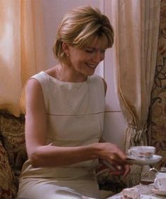 a woman sitting at a table with tea cups and saucers in front of her