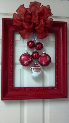 a red frame hanging on the wall with christmas ornaments in front of it and a bow