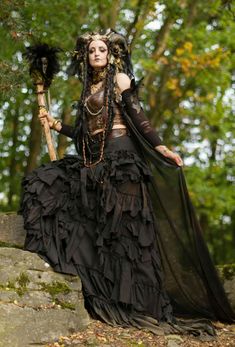 a woman dressed in black is holding a stick and wearing a costume with feathers on it