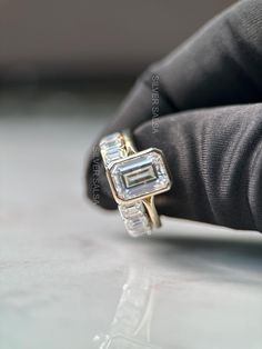 a close up of a person's hand holding a ring with a baguette on it