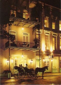 a horse drawn carriage parked in front of a tall building at night with lights on