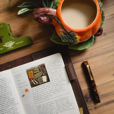 an open book sitting on top of a wooden table next to a cup of coffee