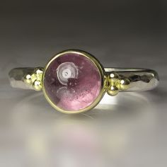 Beautiful, natural spinel cabochon set in 18k bezel on hammered sterling silver band(approx. 2.5mm wide x 1.5mm thick). The spinel has a backsheet of polished fine silver(closed setting). Classic 18k gold granule clusters on each side of the spinel. The spinel measures approx. 7mm in diameter X 5mm deep and weighs 2.63cts.  All metal is from recycled sources. This ring is a size 6 3/4 and I cannot resize. Attractively boxed. Photos have been taken up close for detail. Please refer to dimensions. Yellow Gold Cabochons With Bezel Setting For Gift, Yellow Gold Cabochons With Bezel Setting, Gold Round Cabochons With Bezel Setting, Gold Moonstone Ring With Bezel Setting In Sterling Silver, Fine Jewelry Round Cabochons With Bezel Setting, Round Fine Jewelry Cabochons With Bezel Setting, Round Cabochons With Bezel Setting Fine Jewelry, Sterling Silver Yellow Gold Cabochon Ring, Sterling Silver Ring With Yellow Gold Cabochon