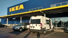 a white van parked in front of a ikea store next to a silver car