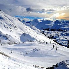 skiers on the top of a snowy mountain with mountains in the backgroud