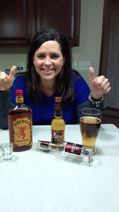 a woman sitting at a table with two bottles of liquor and three shot glasses on it