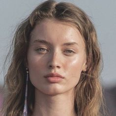 a woman with long hair and earrings on her neck looking off to the side while standing in front of a building