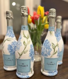 three bottles of champagne sitting on top of a wooden table next to a vase filled with flowers