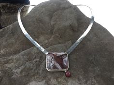 I cut this stone from a slab of unknown jasper I had in my stash. At first I thought it would be a simple pendant. But as I was choosing how to orient it, it occurred to me that it needed to be a torque that carried the lines out from the stone. Made from hammered sterling, it sits just below the clavicle. To finish the form, a high dome opaque ruby with a touch of a star in the perfect color was added below the branch. A unique and eye catching piece. Unique Rectangular Natural Stone Necklace, Unique Rectangular Necklaces With Natural Stones, Unique Jasper Jewelry With Large Pendant, Unique Jasper Necklace With Large Pendant, Hand Forged Agate Pendant Necklace, Hand-forged Agate Pendant Necklace, Unique Rectangular Gemstone Necklace, Artisan Jasper Necklace With Large Stone, Artisan Square Pendant Gemstone Necklace