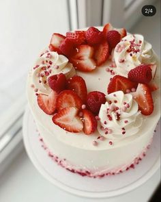 a white cake topped with strawberries and sprinkles next to a window