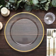 a place setting with gold rimmed plates and silverware on a wooden table top