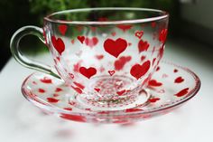 a glass cup and saucer with hearts painted on the inside is sitting on a table