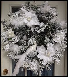 a wreath with white flowers and feathers hanging on the front door, surrounded by snowflakes