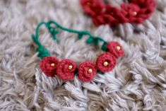 two crocheted flowers are laying on a gray blanket with green string and gold beads