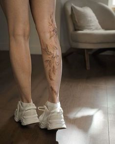 a woman's legs with tattoos on them and white shoes in front of a couch