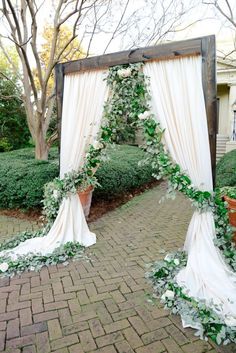 a wedding arch decorated with greenery and white draping for an outdoor ceremony