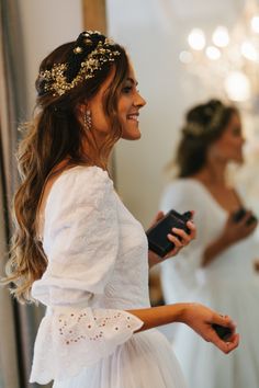 a woman in a white dress is smiling and holding a cell phone while looking at her reflection