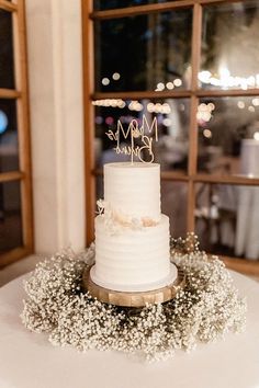 a white wedding cake sitting on top of a table next to an open window with the words mr and mrs written on it