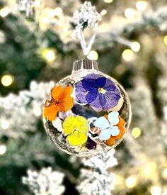 a glass ornament with flowers hanging from it's side in front of a christmas tree