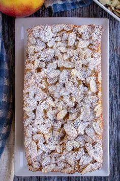 a square cake with powdered sugar on top next to an apple and other fruit